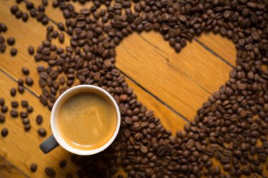 Espresso bardağı ve kahve çekirdekleri ahşap bir zeminde kalp şeklinde..