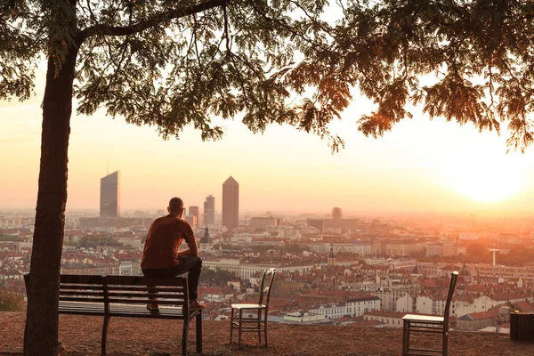 Bir bankta şehrin üzerinde sonbahar gündoğumunun tadını çıkaran bir adam. Lyon, Fransa.
