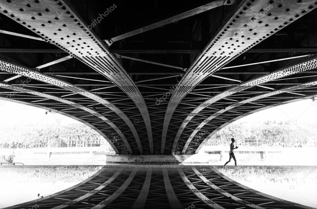 Woman running under a bridge on a warm, summer morning. Lyon, France.