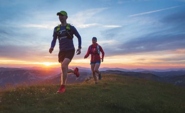 Gün batımında tepelerde koşan iki sporcu. Sığ D.O.F. Ve hareket bulanıklığıyla.