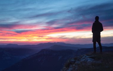 Dağlık bir çölde pembe bir günbatımına bakan yürüyüşçü..