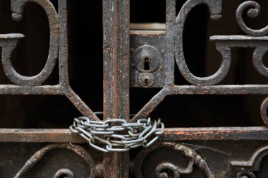 Karanlık bir sokakta paslı bir kapı, etrafı zincirle çevrili..
