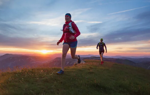 Gün batımında tepelerde koşan iki sporcu. Sığ D.O.F. Ve hareket bulanıklığıyla.