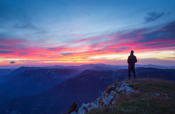 Bir yürüyüşçü dağlık bir arazide pembe bir günbatımına bakıyor..