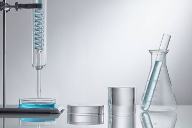 Laboratuvar ekipmanlarında cam kaidesi üzerine sahne vitrini kozmetiği. Beyaz arka planda mavi su içerikli laboratuvar cam ekipmanları. Araştırma ve geliştirme kozmetik konsepti