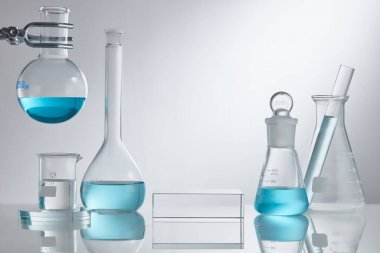 Laboratuvar ekipmanlarında cam kaidesi üzerine sahne vitrini kozmetiği. Beyaz arka planda mavi su içerikli laboratuvar cam ekipmanları. Araştırma ve geliştirme kozmetik konsepti