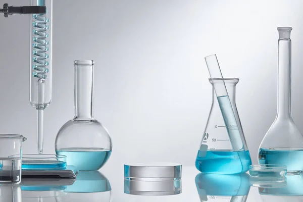 在实验室设备的现代玻璃基座上展示化妆品 实验室玻璃设备 白色底座上有蓝色水成份 研究与开发化妆品概念 — 图库照片