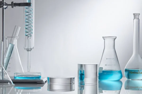 Stage showcase cosmetics on glass pedestal modern in laboratory equipment. Laboratory glass equipment with blue water ingredients on white background. Research and development cosmetics concept