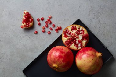 Olgun nar meyvesi ve yarım nar tohumu, gri beton arka planda yapraklı nar tohumu. Beyaz tabakta taze nar var. Vegan, sağlıklı beslenme konsepti. Üst görünüm.