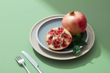 Kırmızı nar meyvesi, tohum, yarısı açık yeşil arka planlı pastel tabakta..