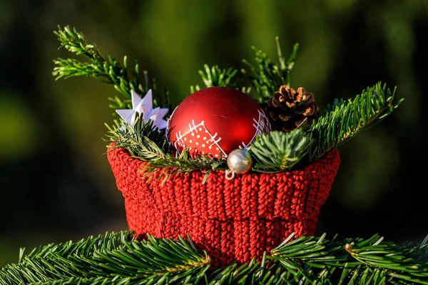 A red crocheted basket with fir branches and a red Christmas tree ball against a green background
