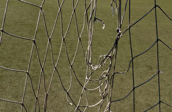 Aufgerissenes Fußballnetz gegen grünen Rasenplatz. — Stockfoto