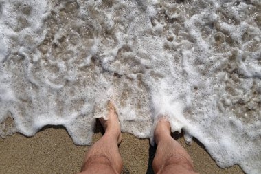 İnsan ayağı, deniz dalgası ve kum. Seyahat sahnesi ve arkaplan        