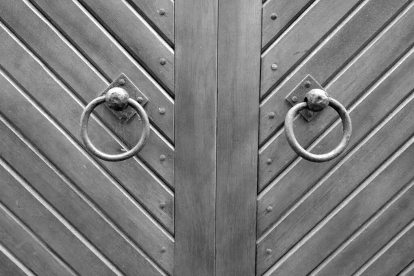 Old metal door hinge on wooden door in black and white. Abstract background and texture for design.