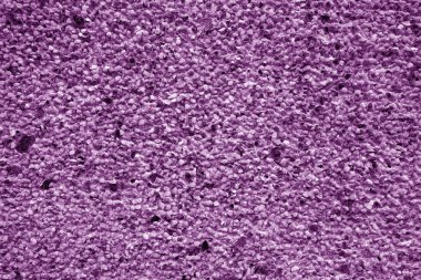 Mor tonda küçük taşlarla kaplı duvar. Pis ve yıpranmış arka plan.