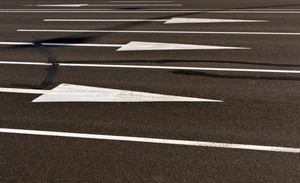 Białe strzałki i linie na powierzchni pęknięty asfalt. — Zdjęcie stockowe
