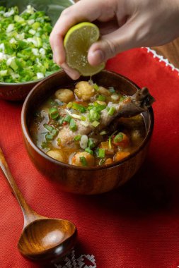 Geleneksel Vori Vori çorbasına vori vori topları ve tavukla taze limon suyu ekleyen kişi, kırmızı Aopo 'i el yapımı dantel masa örtüsü ve otantik Paraguay mutfağında servis ediliyor..