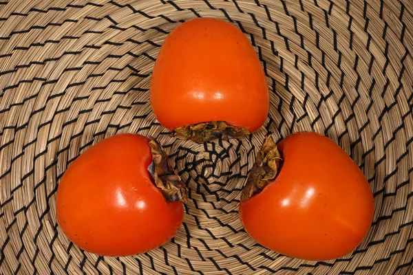 Hasır arka plan açık kahverengi üzerinde üç fetal Trabzon hurması