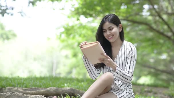 Jovem mulher atraente ler livro pela árvore no parque — Vídeo de Stock