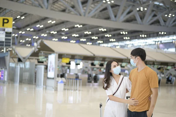 An Asian couple is wearing protective mask in International airport, travel under Covid-19 pandemic, safety travels, social distancing protocol, New normal travel concept .
