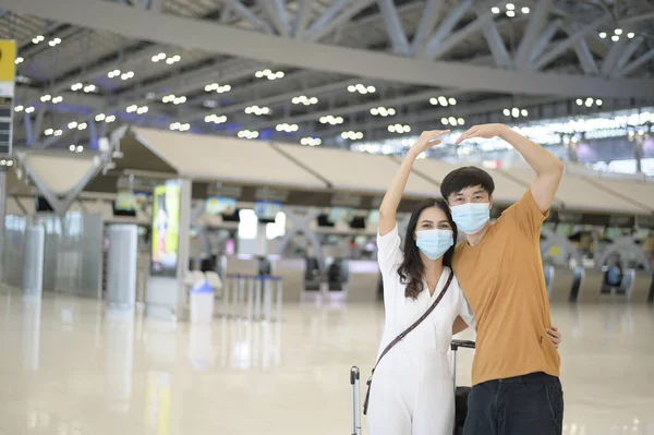 An Asian couple is wearing protective mask in International airport, travel under Covid-19 pandemic, safety travels, social distancing protocol, New normal travel concept .