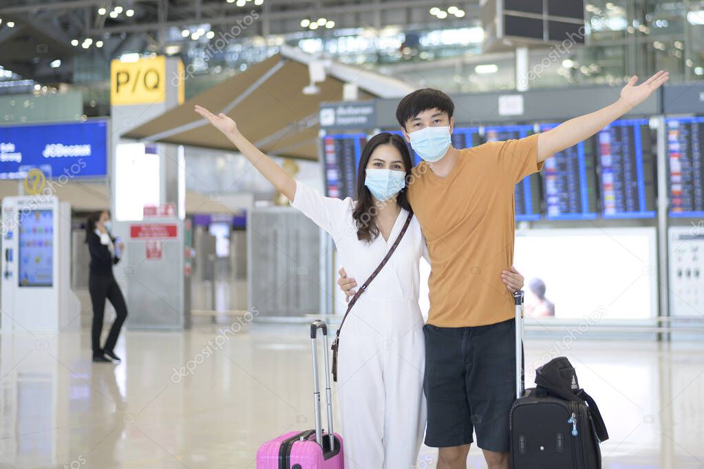 An Asian couple is wearing protective mask in International airport, travel under Covid-19 pandemic, safety travels, social distancing protocol, New normal travel concept .