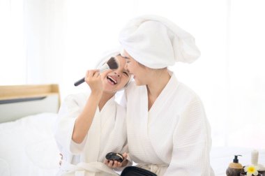 Beyaz bornozlu mutlu bir anne ve kız makyaj malzemesi sürüyor. Kozmetik fırçasıyla, Aile ve Güzellik Konseptiyle.. 