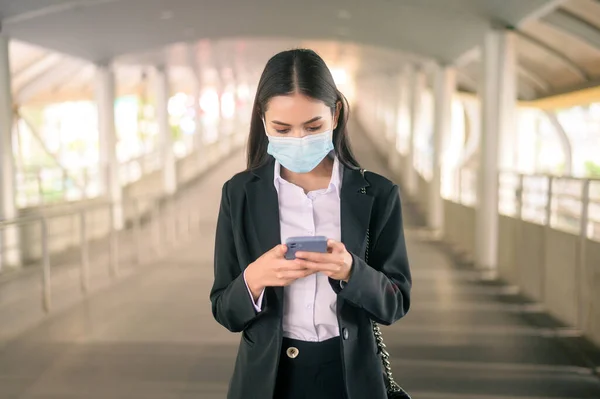 Young business woman with face mask  is standing on metro platform using smart.