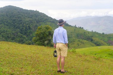 Yağmur mevsiminde, tropikal iklimde, güzel yeşil dağ manzarasının keyfini çıkaran ve rahatlatan gezgin bir adam..