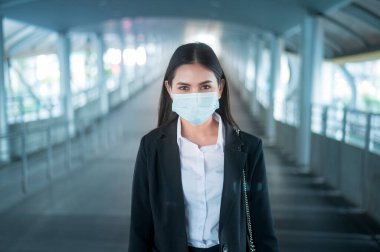 Yüzü maskeli genç bir iş kadını metro platformunda akıllı bir şekilde duruyor.. 