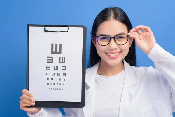 青い背景のスタジオ 医療の概念上の目のチャートを保持眼鏡を持つ若い女性眼科医 — ストック写真