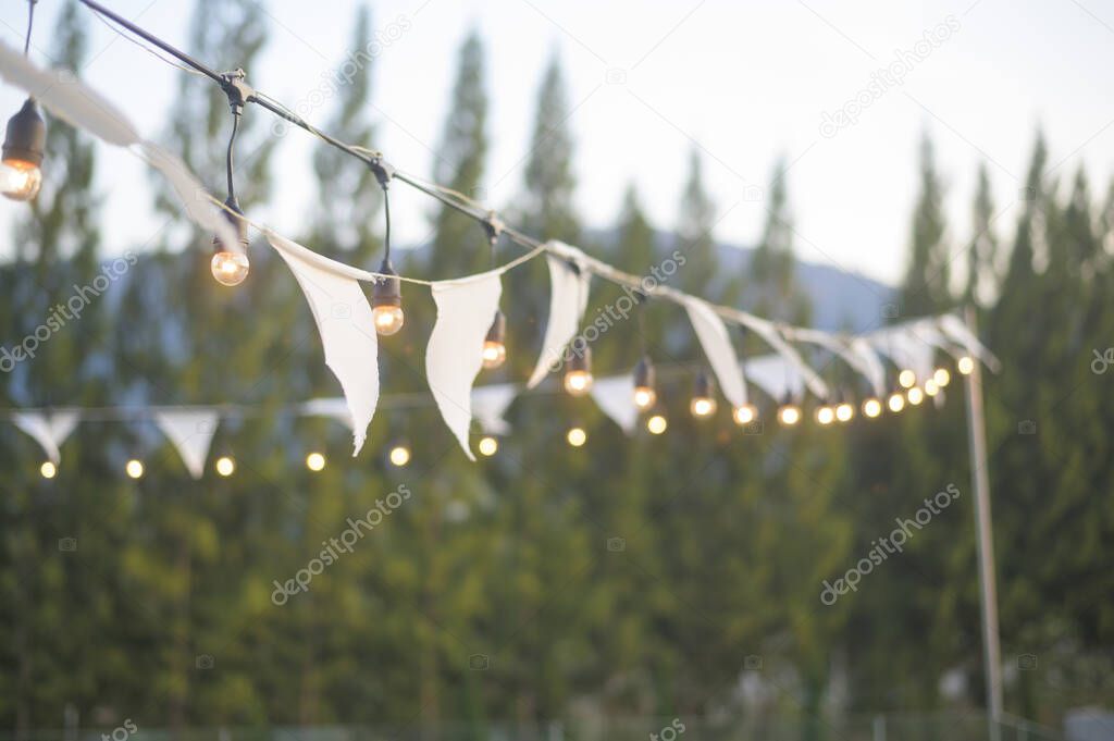 Warm lighting Festival decorative string lights hang and glow outdoors at night.