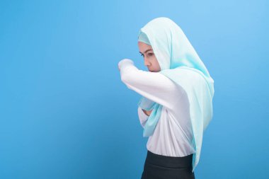 Başörtüsü olan genç Müslüman kadın kendini hasta hissediyor ve mavi arka plan stüdyosunda öksürüyor