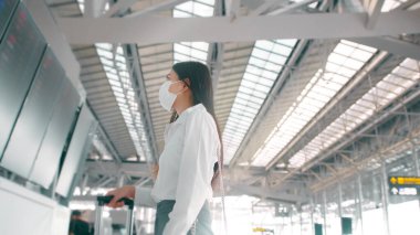 Uluslararası havaalanında koruyucu maske takan bir iş kadını Covid-19 salgını, güvenlik seyahati, sosyal mesafe protokolü, yeni normal seyahat kavramı altında seyahat ediyor.