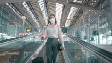 Uluslararası havaalanında koruyucu maske takan bir iş kadını Covid-19 salgını, güvenlik seyahati, sosyal mesafe protokolü, yeni normal seyahat kavramı altında seyahat ediyor.