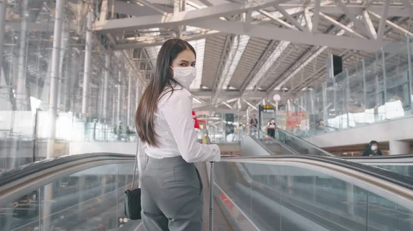 A business woman is wearing protective mask in International airport, travel under Covid-19 pandemic, safety travels, social distancing protocol, New normal travel concept