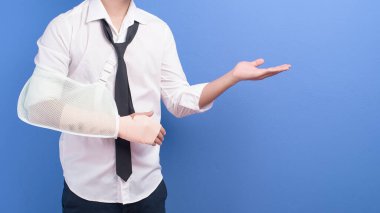 Stüdyo, sigorta ve sağlık hizmetleri konseptinde mavi arka planda yaralı bir kolu olan genç bir işadamı.