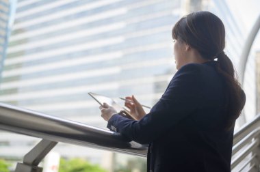 Güzel Asyalı genç iş kadını modern şehirde tablet kullanıyor.  