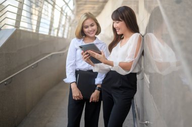 Mutlu gülümseyen genç iş kadınları modern şehirde iş planı hakkında konuşuyorlar.