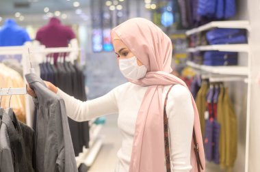 Alışveriş merkezinde koruyucu maske takan genç bir Müslüman kadın Covid-19 pandemik konsept altında alışveriş yapıyor..