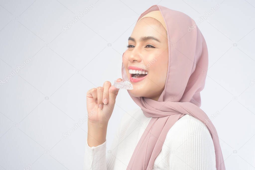 A young muslim woman holding invisalign braces over white background studio, dental healthcare and Orthodontic concept.