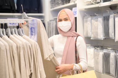 Alışveriş merkezinde koruyucu maske takan genç bir Müslüman kadın Covid-19 pandemik konsept altında alışveriş yapıyor..