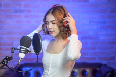 Renkli ışıklarla dolu bir müzik stüdyosunda şarkı söylerken mikrofonla kulaklık takan genç bir bayan şarkıcı..