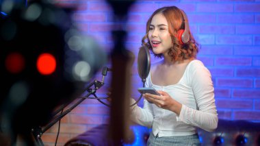 Renkli ışıklarla dolu bir müzik stüdyosunda şarkı söylerken mikrofonla kulaklık takan genç bir bayan şarkıcı..