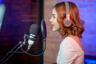 Renkli ışıklarla dolu bir müzik stüdyosunda şarkı söylerken mikrofonla kulaklık takan genç bir bayan şarkıcı..