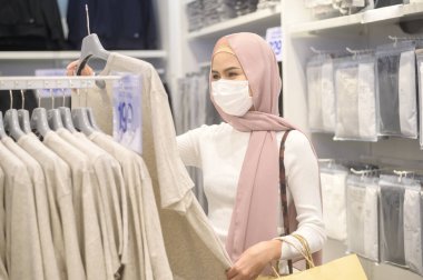 Alışveriş merkezinde koruyucu maske takan genç bir Müslüman kadın Covid-19 pandemik konsept altında alışveriş yapıyor..