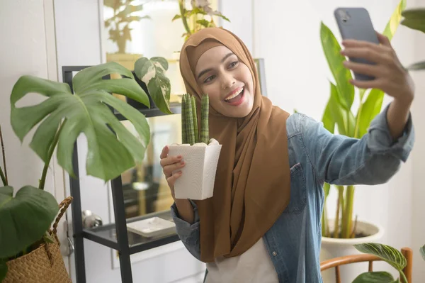 Genç ve mutlu bir müslüman kadın bitkileriyle selfie çekiyor ve evde video görüşmesi yapıyor. 
