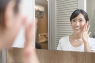 Mutlu güzel bir kadın yüzüne nemlendirici krem sürüyor, cilt bakımı ve tedavi konsepti.