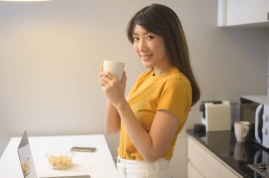 Dizüstü bilgisayarıyla çalışan ve bir fincan kahve içen genç bir kadın, yaşam tarzı ve iş konsepti.