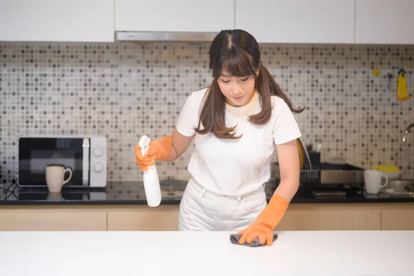 保護ゴム手袋を身に着けている若い美しい女性は自宅でキッチンでテーブルを掃除しています — ストック写真